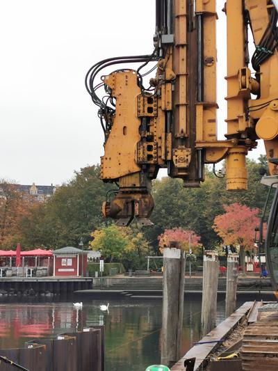 Bild vergrößern: Mit großen Maschinen werden die 14 Meter langen Stahlspundbohlen in Boden eingebracht - die Hafenspitze bleibt bis Januar 2021 Baustelle.
